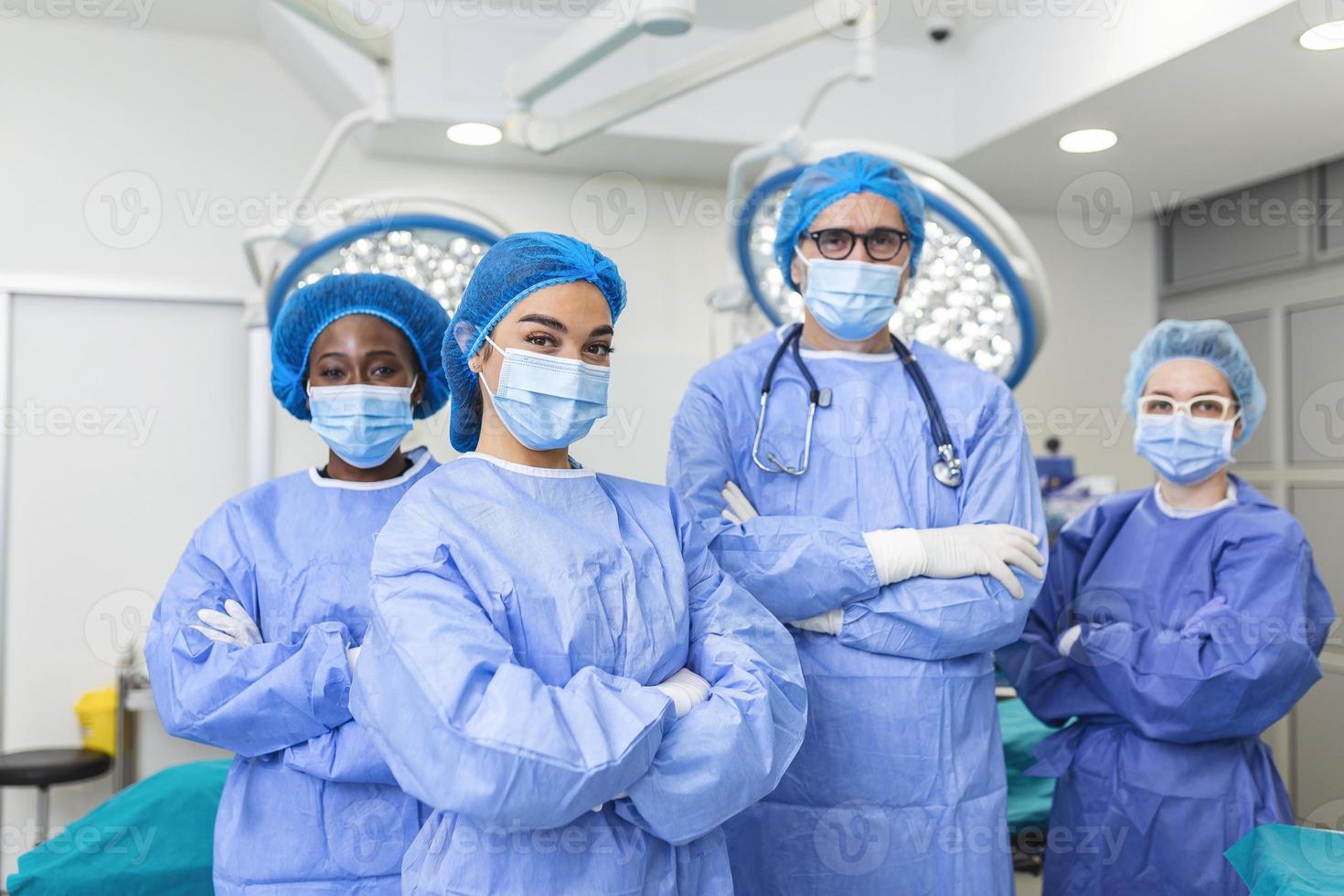 grupo multiétnico de quatro profissionais de saúde, uma equipe de médicos, cirurgiões e enfermeiras, realizando cirurgia em um paciente na sala de cirurgia de um hospital. eles estão olhando para a câmera. foto