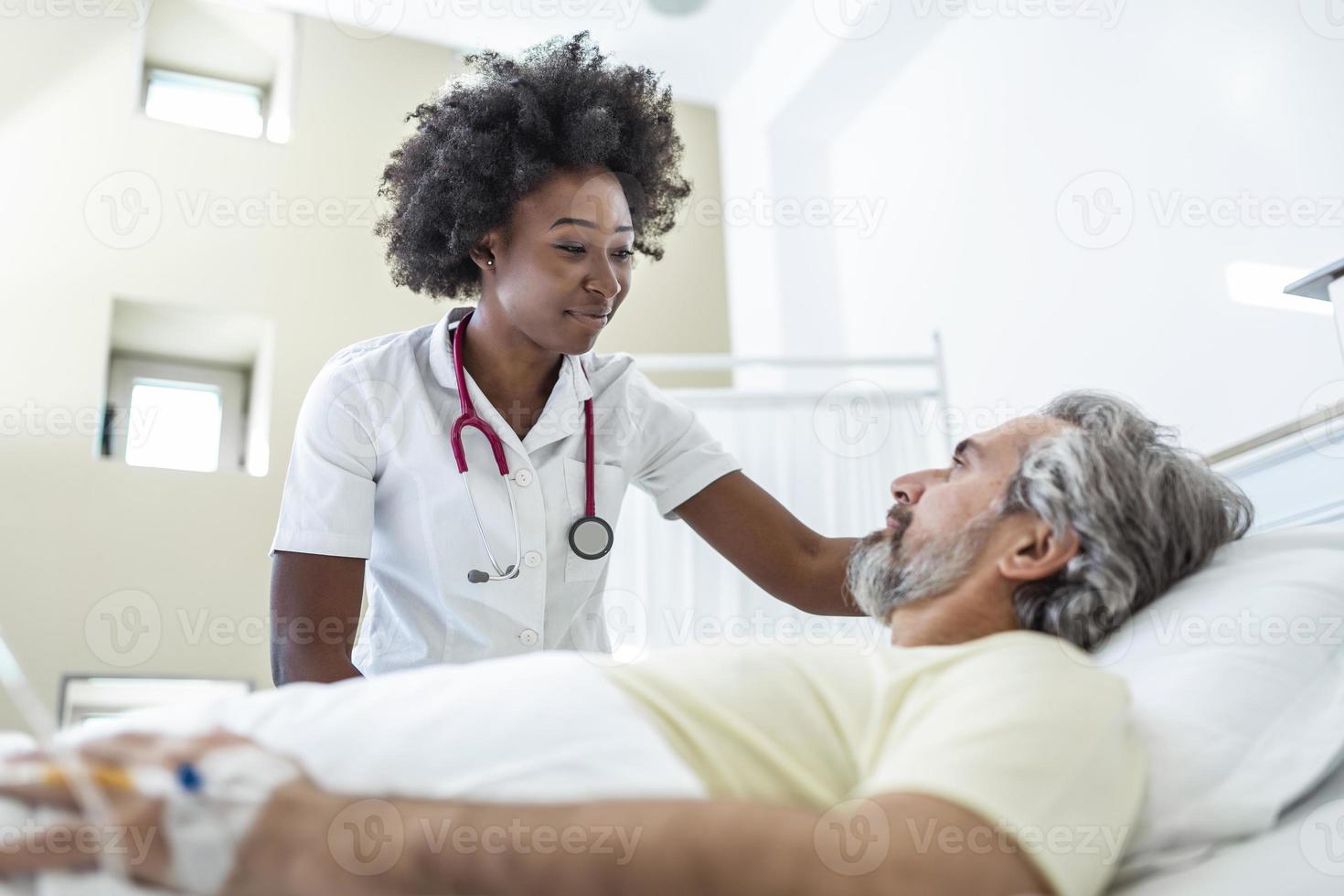 paciente sênior na cama conversando com uma médica afro-americana em quarto de hospital, cuidados de saúde e conceito de seguro. médico reconfortando paciente idoso em cama de hospital ou aconselhando diagnóstico de saúde. foto