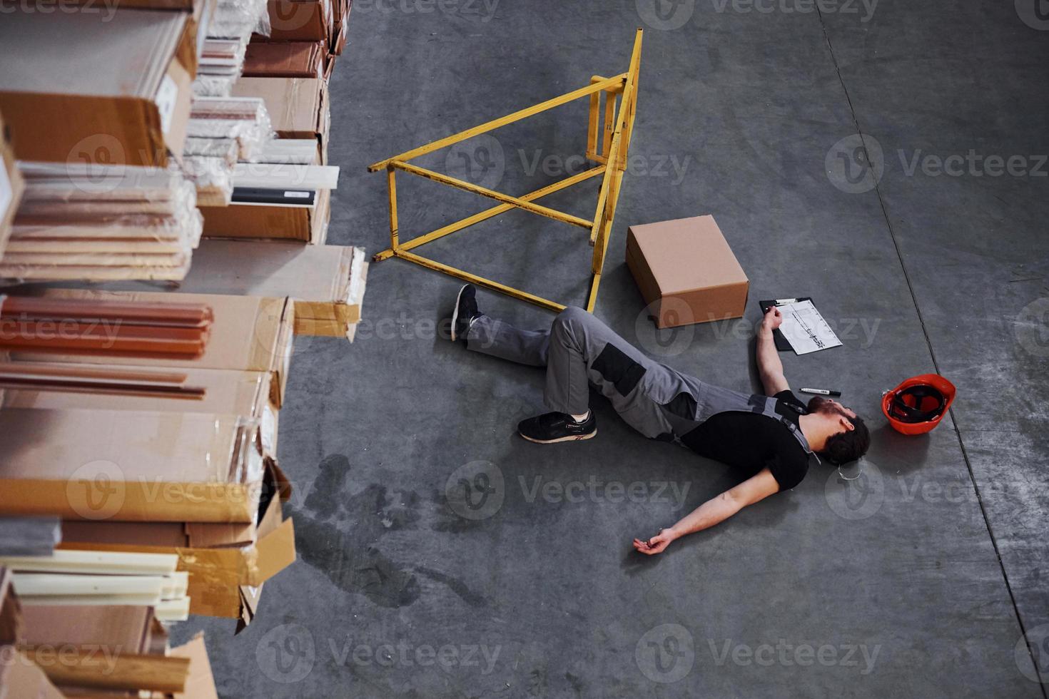 trabalhador do armazém após um acidente no armazenamento. homem de uniforme deitado no chão foto