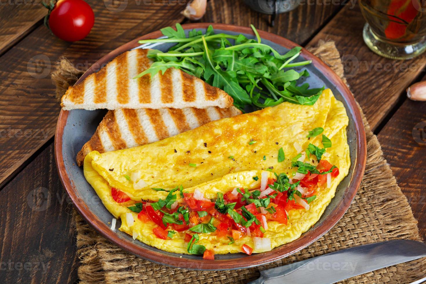 omelete frito com tomate, cebola e ervas. delicioso café da manhã com ovos e torradas foto