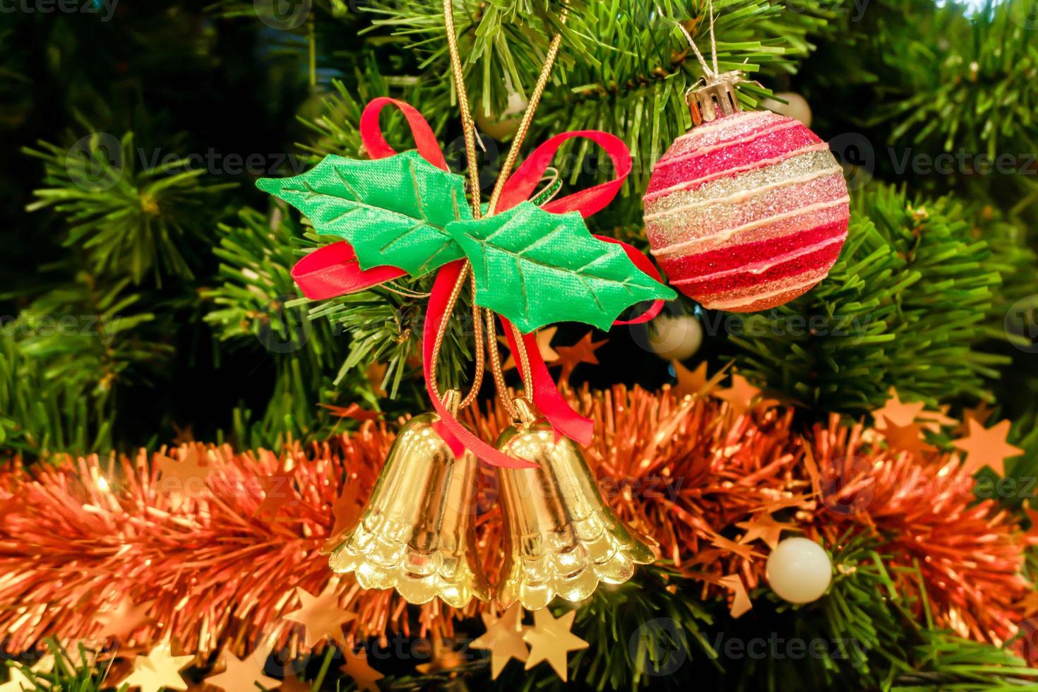 sinos dourados de natal e bola de cristal rosa com enfeites de natal decorados em fundo de pinheiro. foto