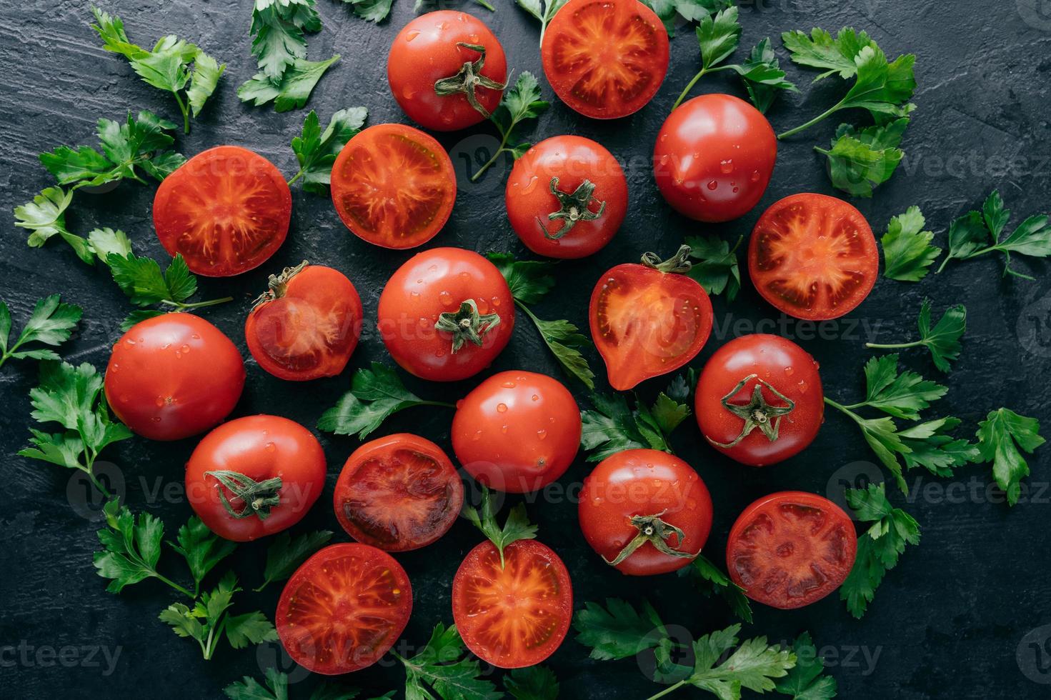 close-up tiro de tomates vermelhos suculentos frescos e salsa verde ao redor em fundo escuro. vegetais de primavera cheios de vitaminas. conceito de nutrição foto