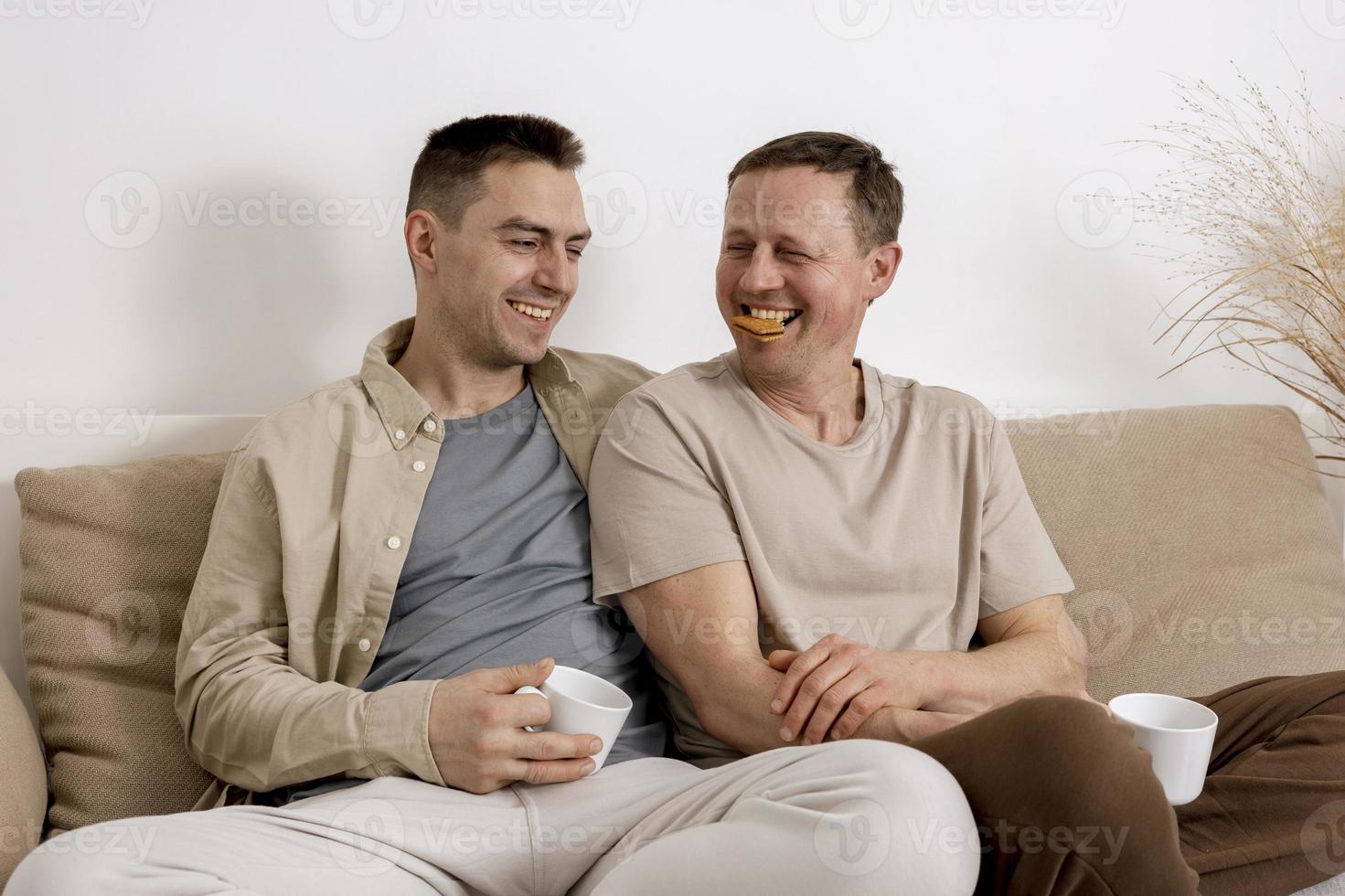 casal gay feliz com roupas casuais passando tempo juntos em casa, assistindo filme no laptop e bebendo chá. dois homens caucasianos relaxantes. relações homossexuais e amor alternativo. foto