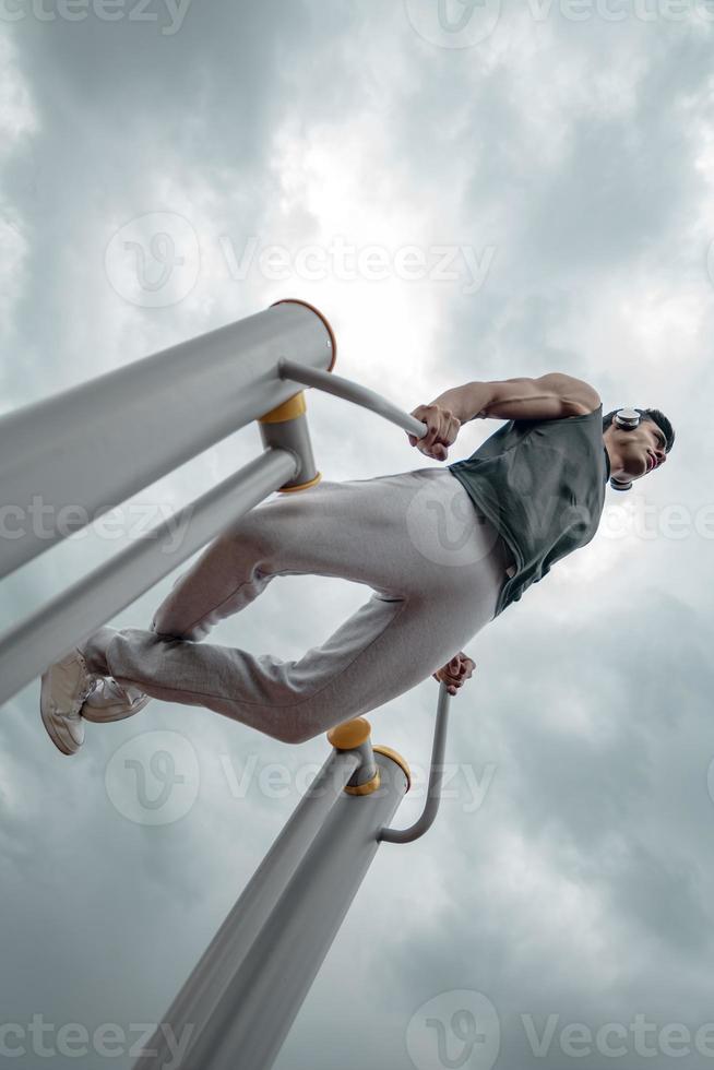 esportista malhando no equipamento público de esportes na academia ao ar livre. um homem ativo esportivo em um parque em dia nublado. foto