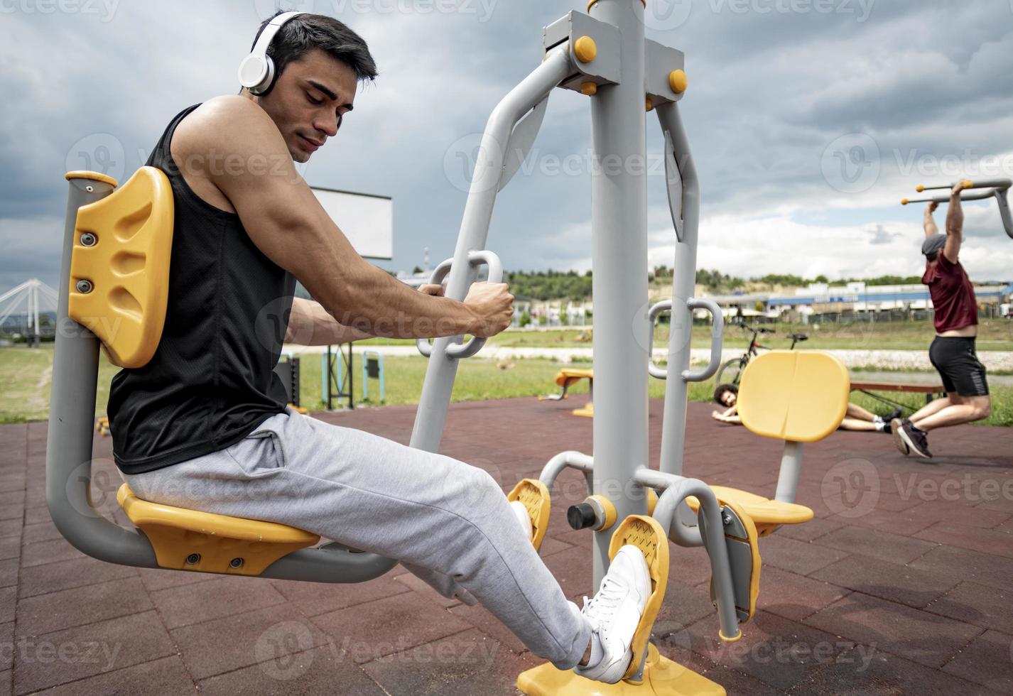 esportista malhando no equipamento público de esportes na academia ao ar livre. um homem ativo esportivo em um parque em dia nublado. foto