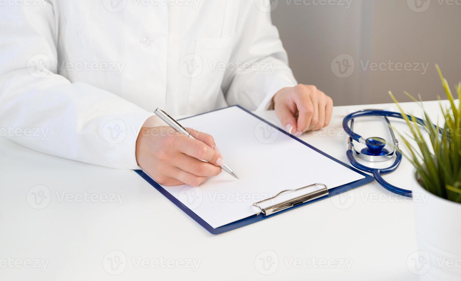 médico irreconhecível fazendo anotações na história da doença com estetoscópio perto foto