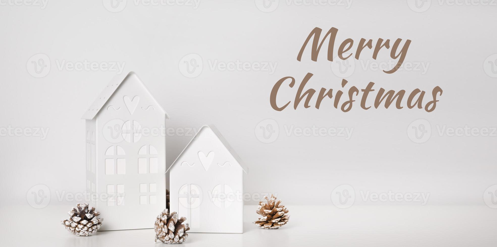 texto de feliz natal com casas de decoração de inverno com luzes perto de pinhas cartão de saudações foto