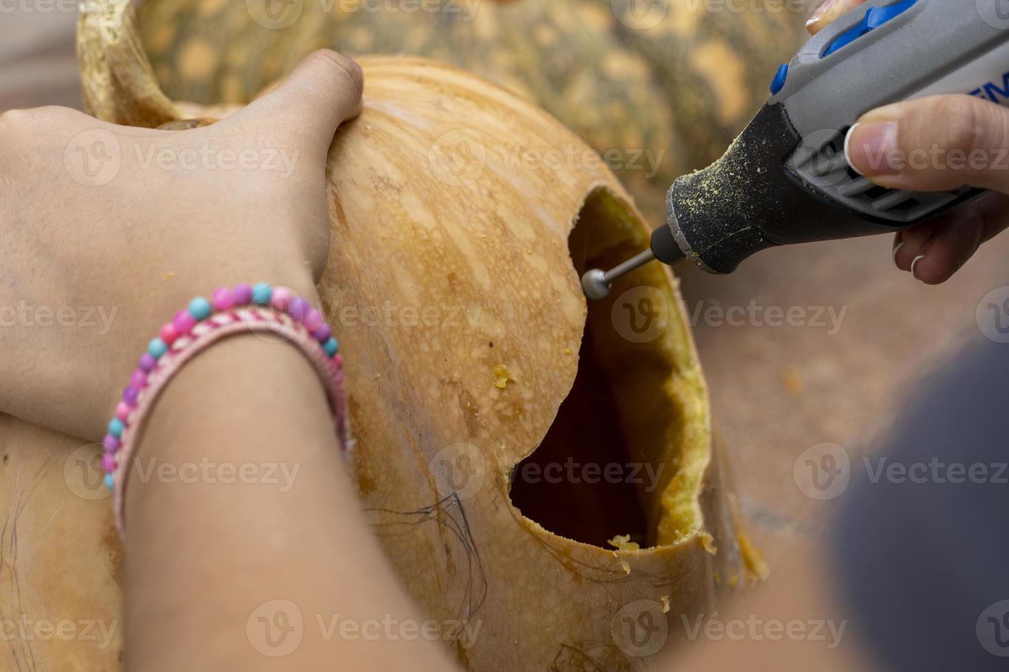 fêmea esculpindo grande abóbora laranja para o halloween enquanto está sentado na mesa de madeira em casa foto