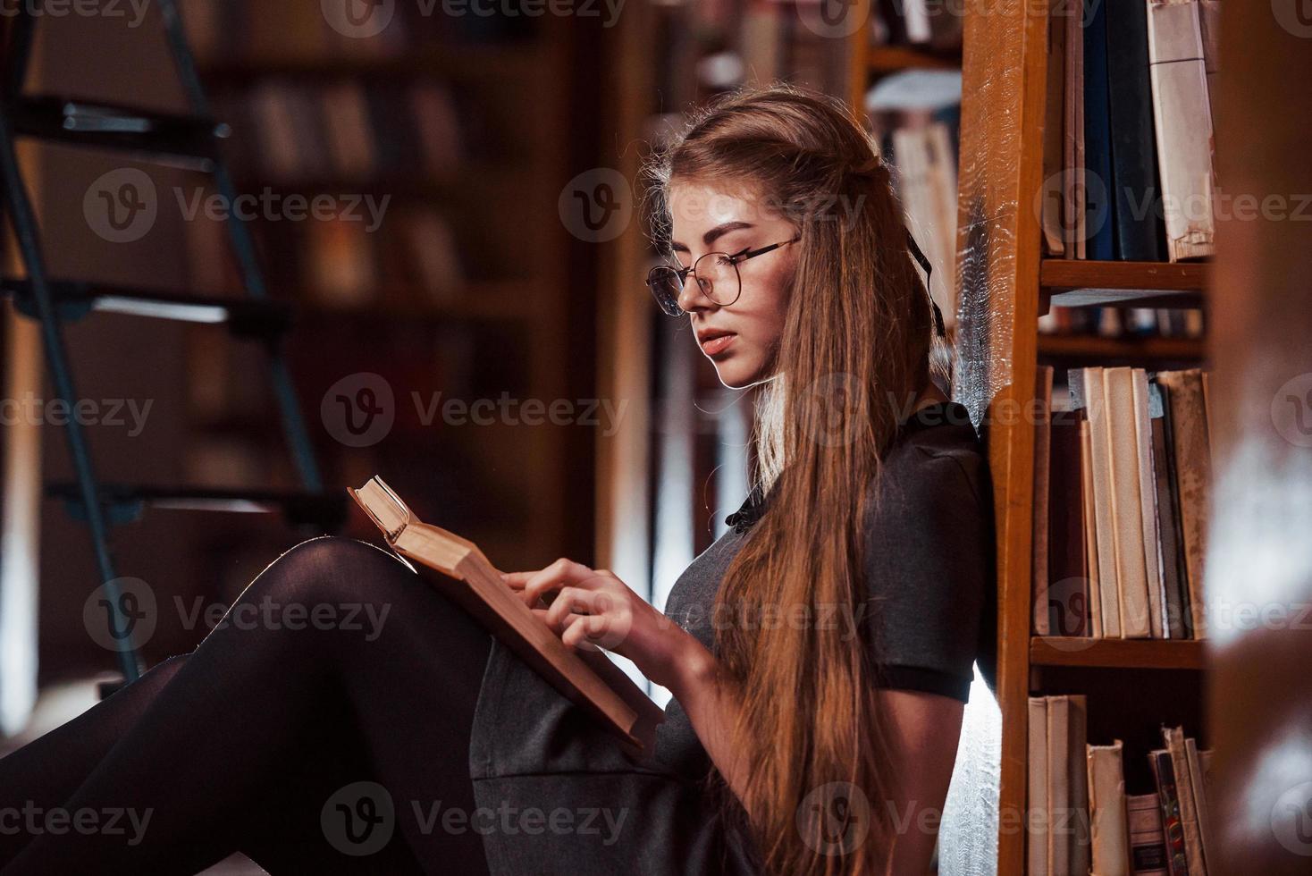 senta no chão. aluna está na biblioteca cheia de livros. concepção de educação foto