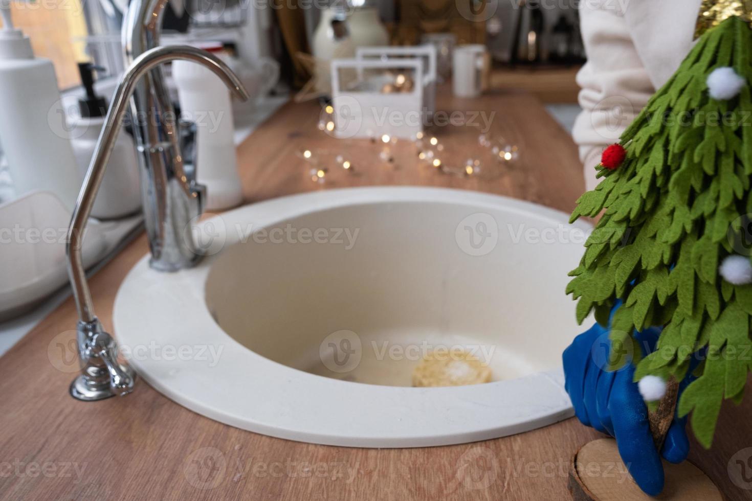 limpando a cozinha antes dos feriados de natal e ano novo. detergente, pó seco, esponja, luvas estão na pia. decoração festiva na cozinha branca, interior aconchegante da casa foto