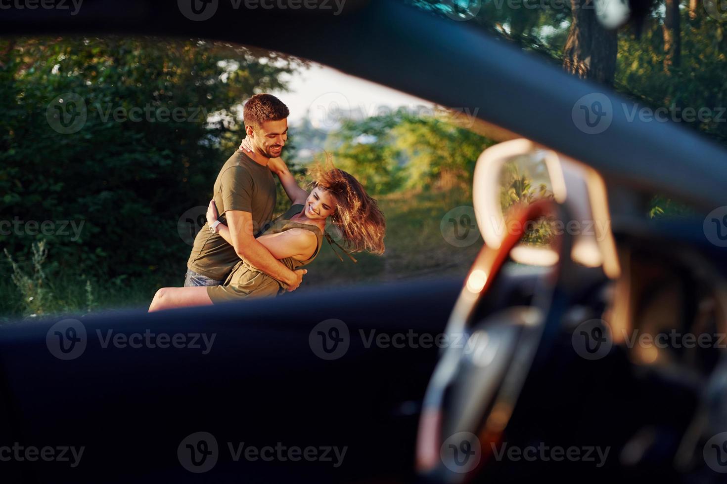 vista pela janela do carro. lindo casal jovem se diverte na floresta durante o dia foto