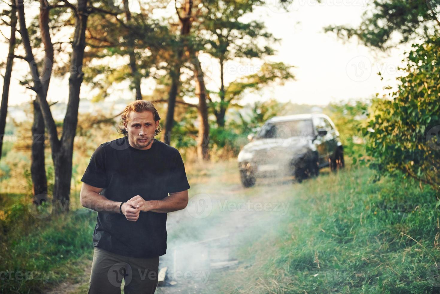 automóvel preto atrás. retrato do homem que fica na floresta e olha para a natureza foto