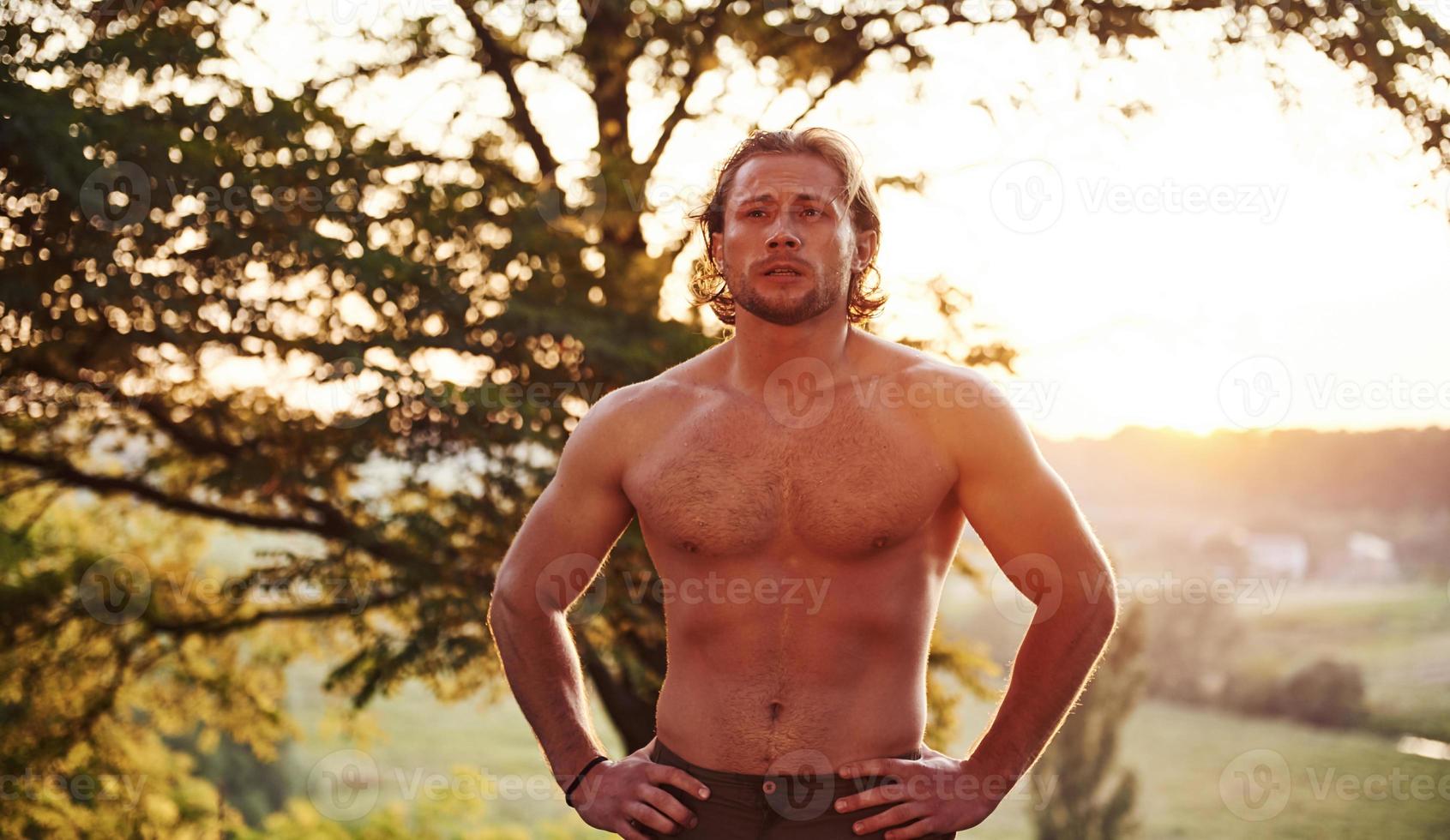 natureza bela. homem bonito sem camisa com tipo de corpo musculoso está na floresta durante o dia foto