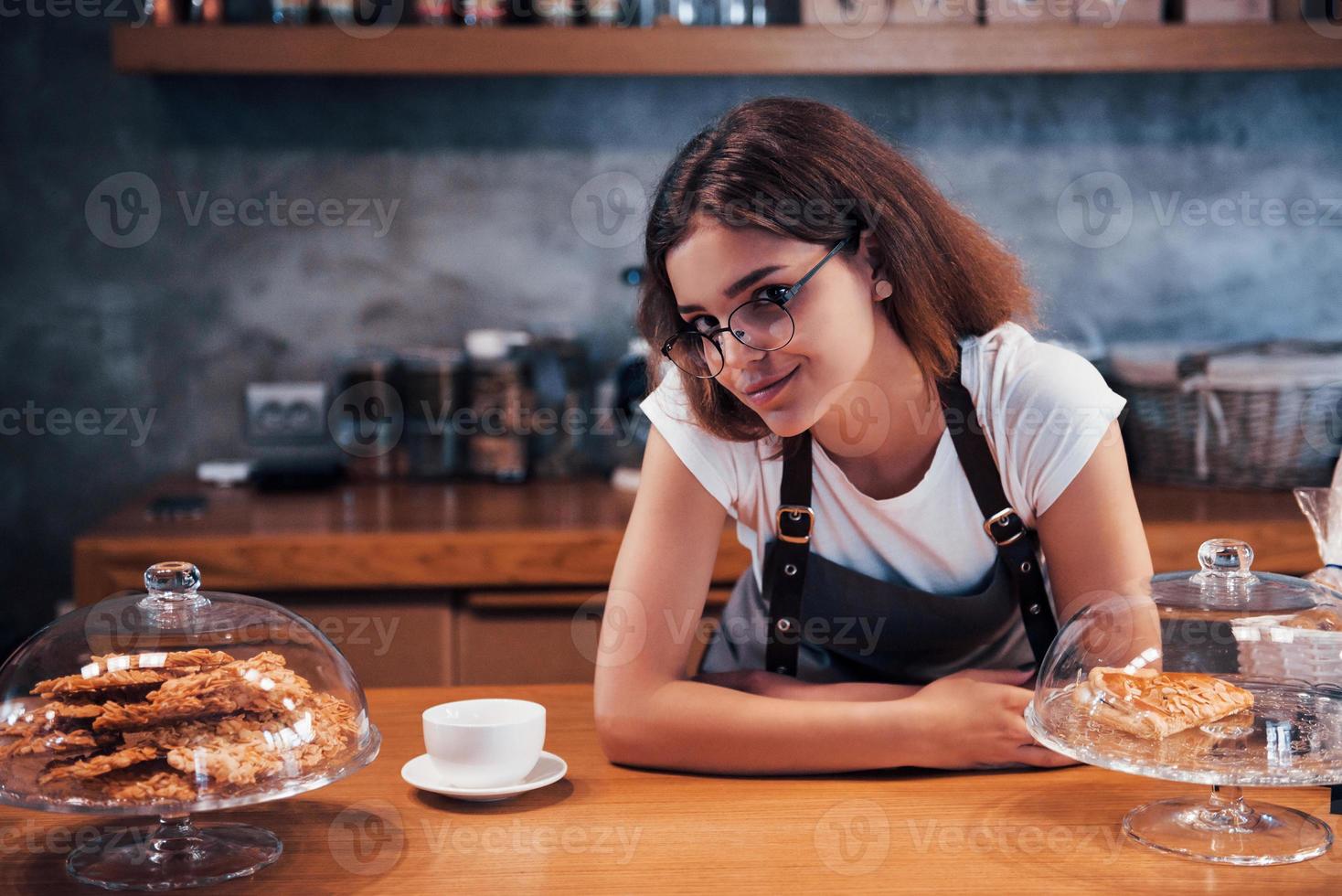 encostado na mesa de madeira. jovem trabalhadora de café feminino dentro de casa. concepção de negócio e serviço foto