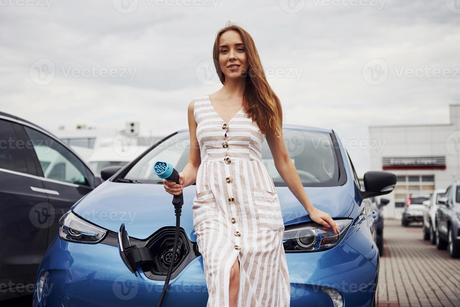 mulher na estação de carga de carros elétricos durante o dia. veículo novo foto