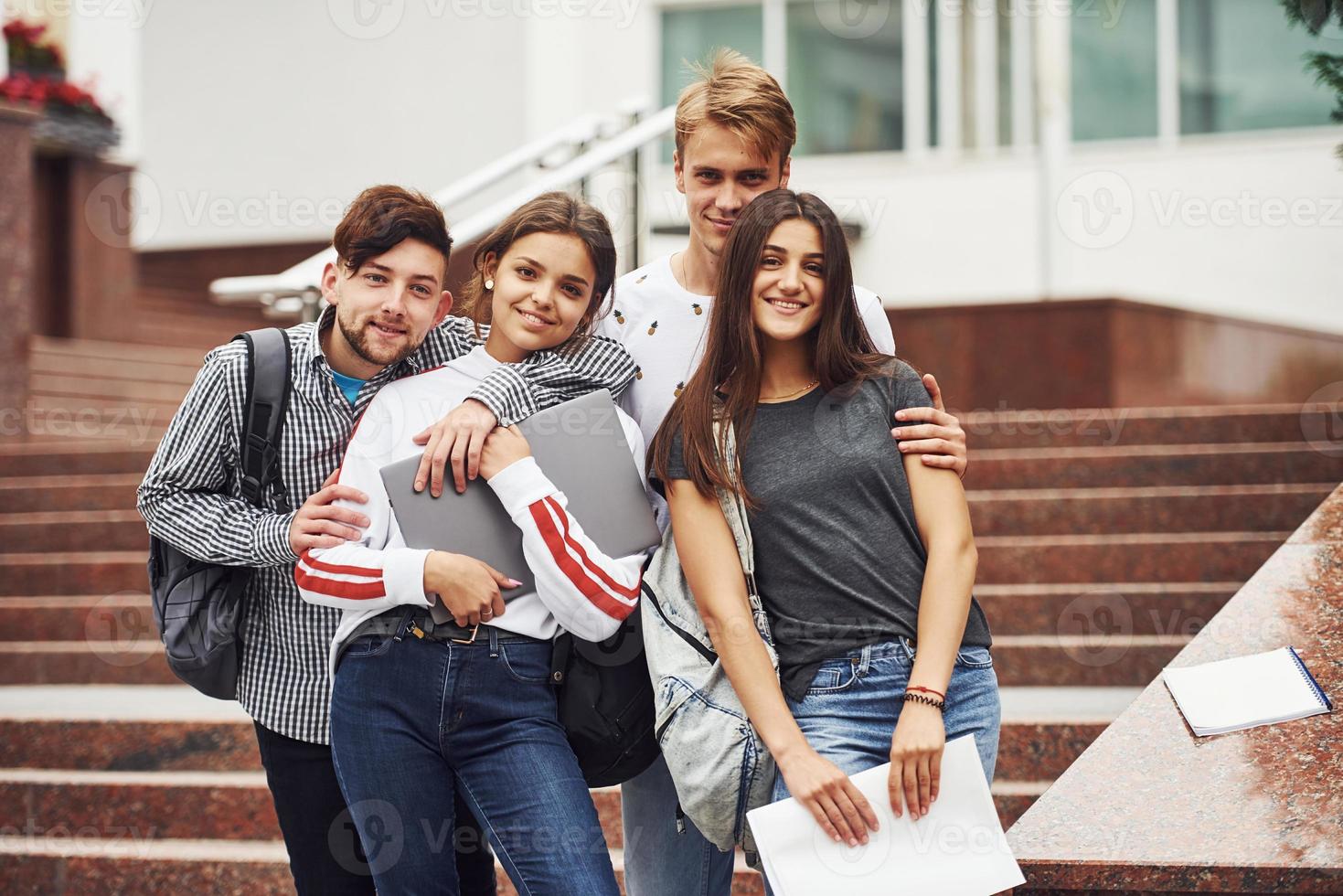 abraçando um ao outro. grupo de jovens estudantes em roupas casuais perto da universidade durante o dia foto