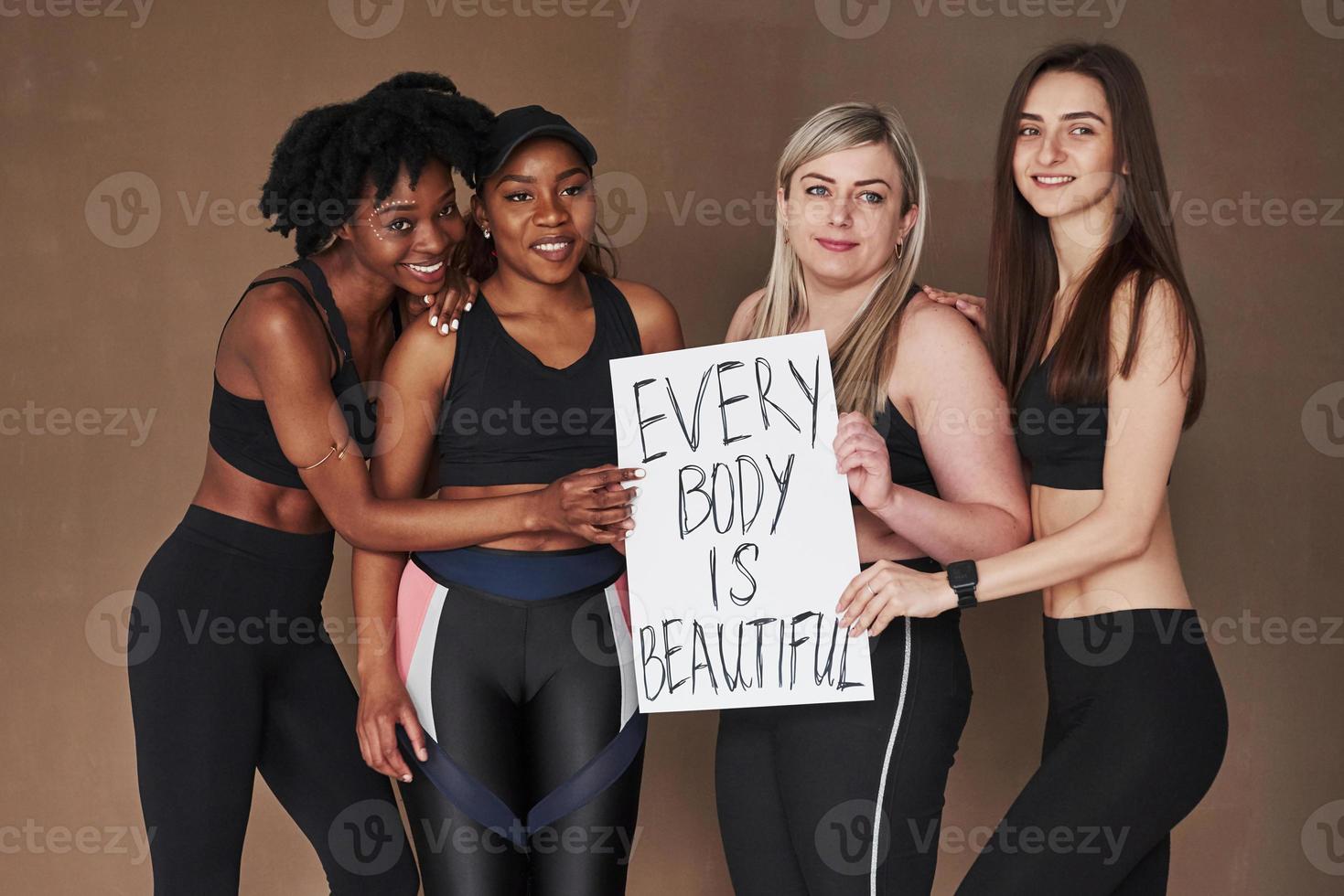 olhando para o lado. grupo de mulheres multiétnicas em pé no estúdio contra fundo marrom foto