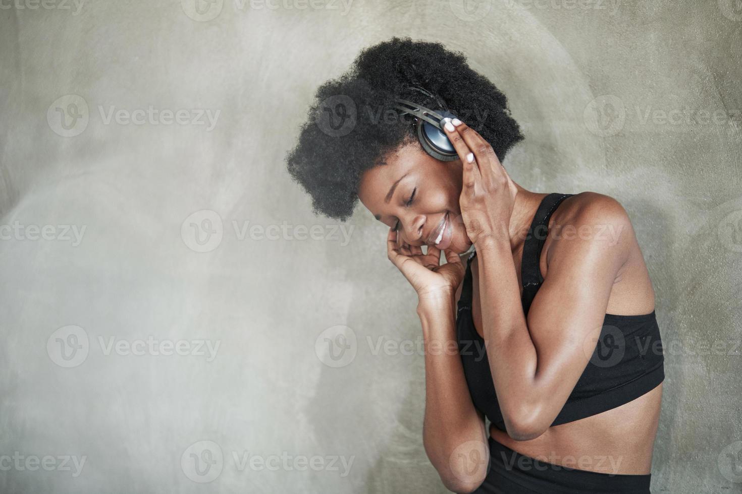 mulher bonita em fones de ouvido. retrato de garota afro-americana em roupas de fitness, tendo uma pausa após o treino foto