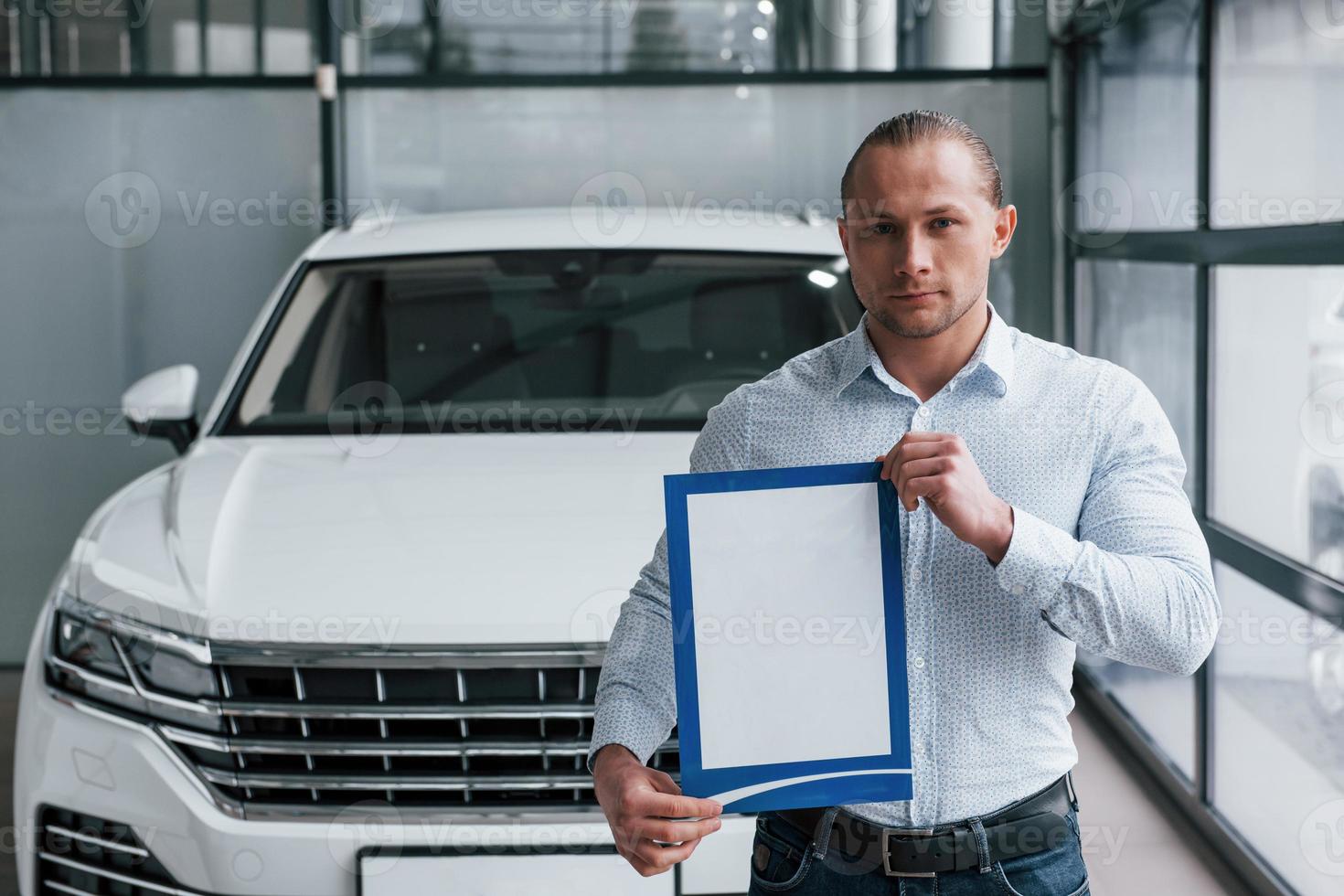 gerente fica na frente do carro branco moderno com papel e documentos nas mãos foto