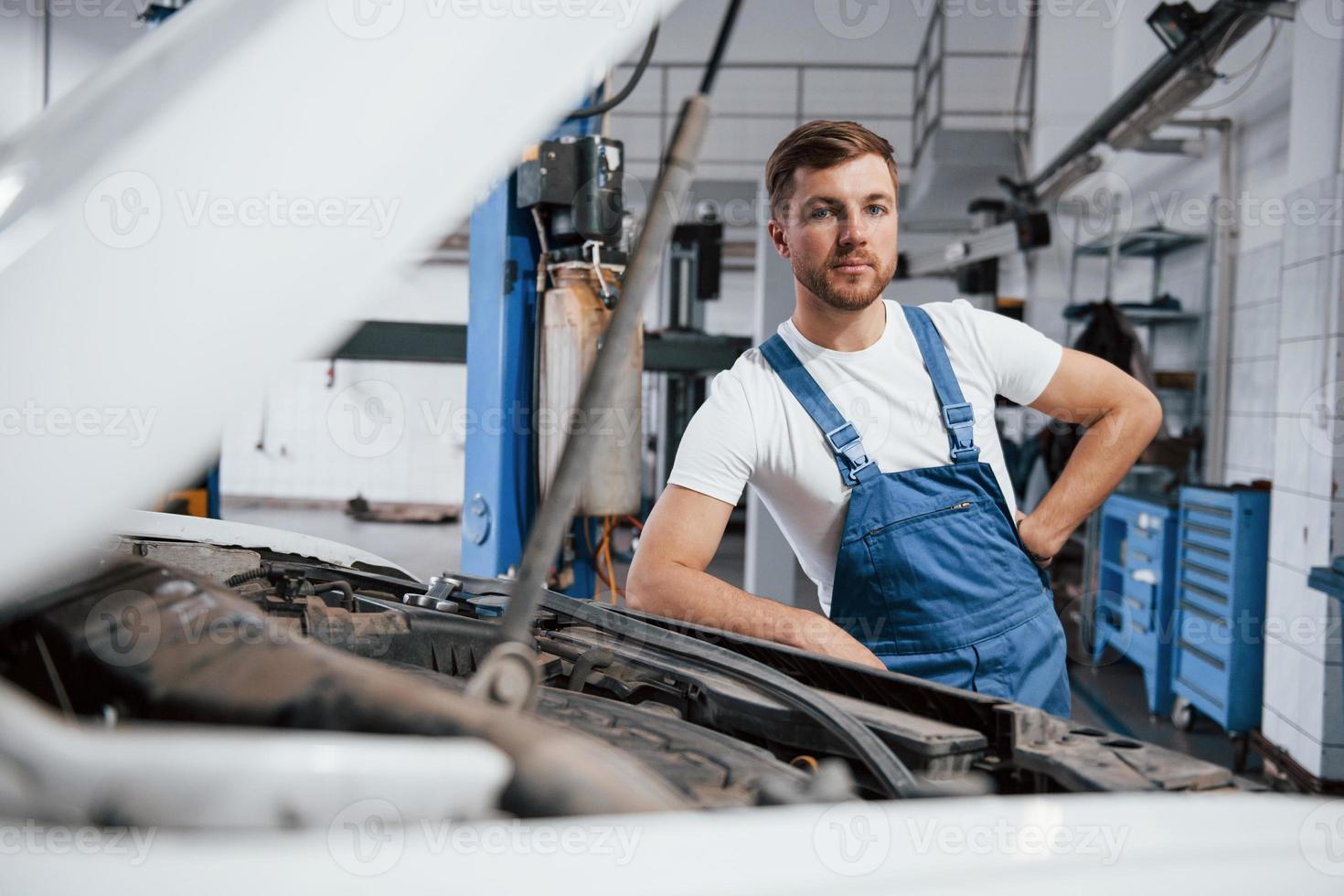 olhando para a câmera. funcionário de uniforme de cor azul trabalha no salão de automóveis foto