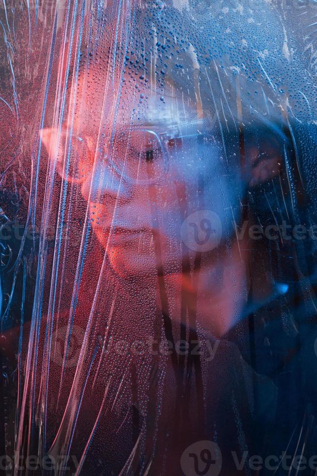 óculos de plástico. studio filmado em estúdio escuro com luz neon. retrato de homem sério por trás do vidro molhado foto