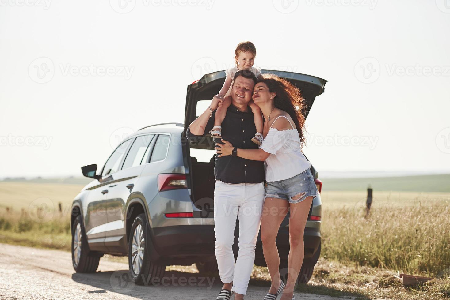 vai andar. a família se diverte no campo perto do automóvel prateado ao pôr do sol foto