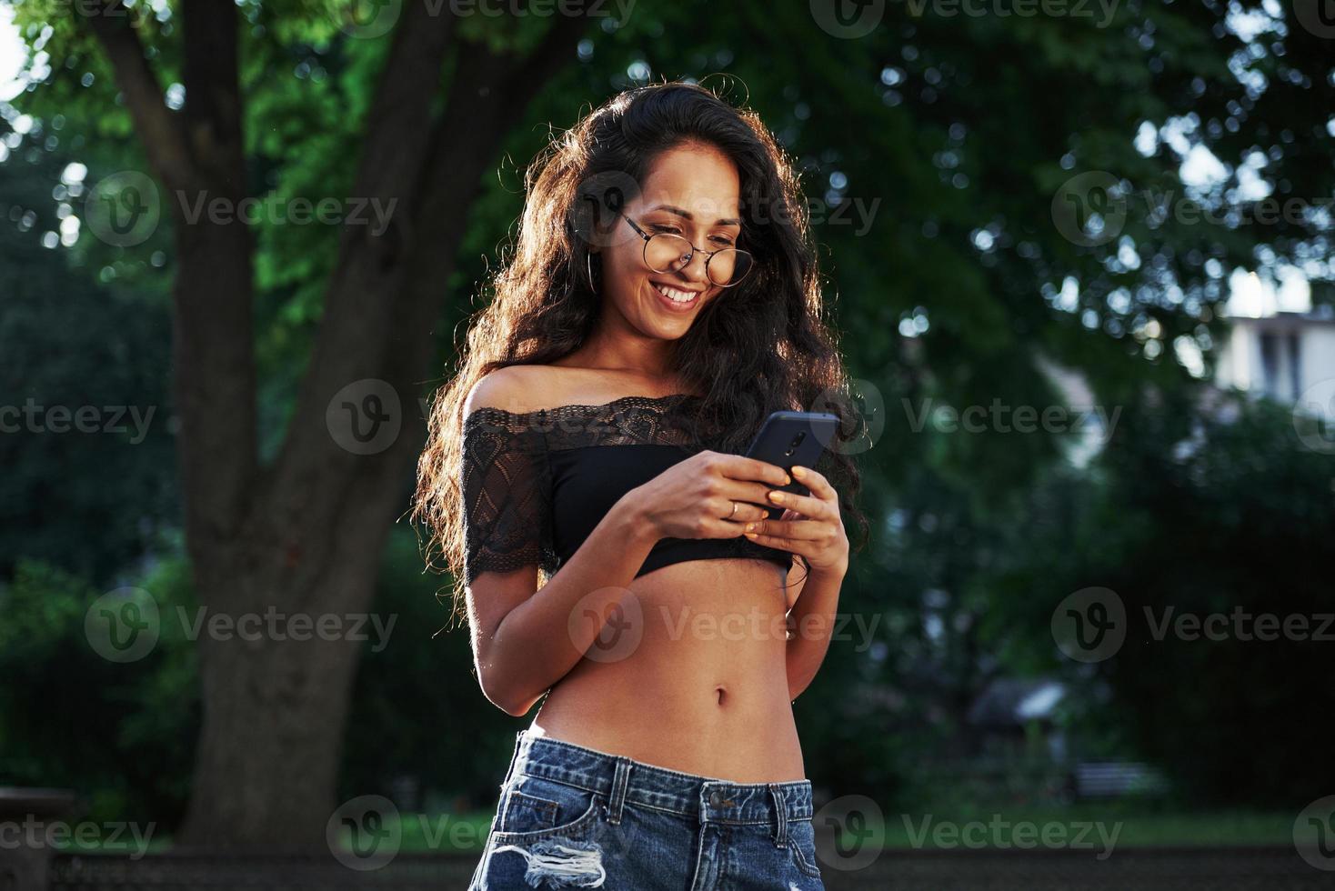 mensagens usando o telefone. mulher bonita com cabelo preto encaracolado se diverte na cidade durante o dia foto