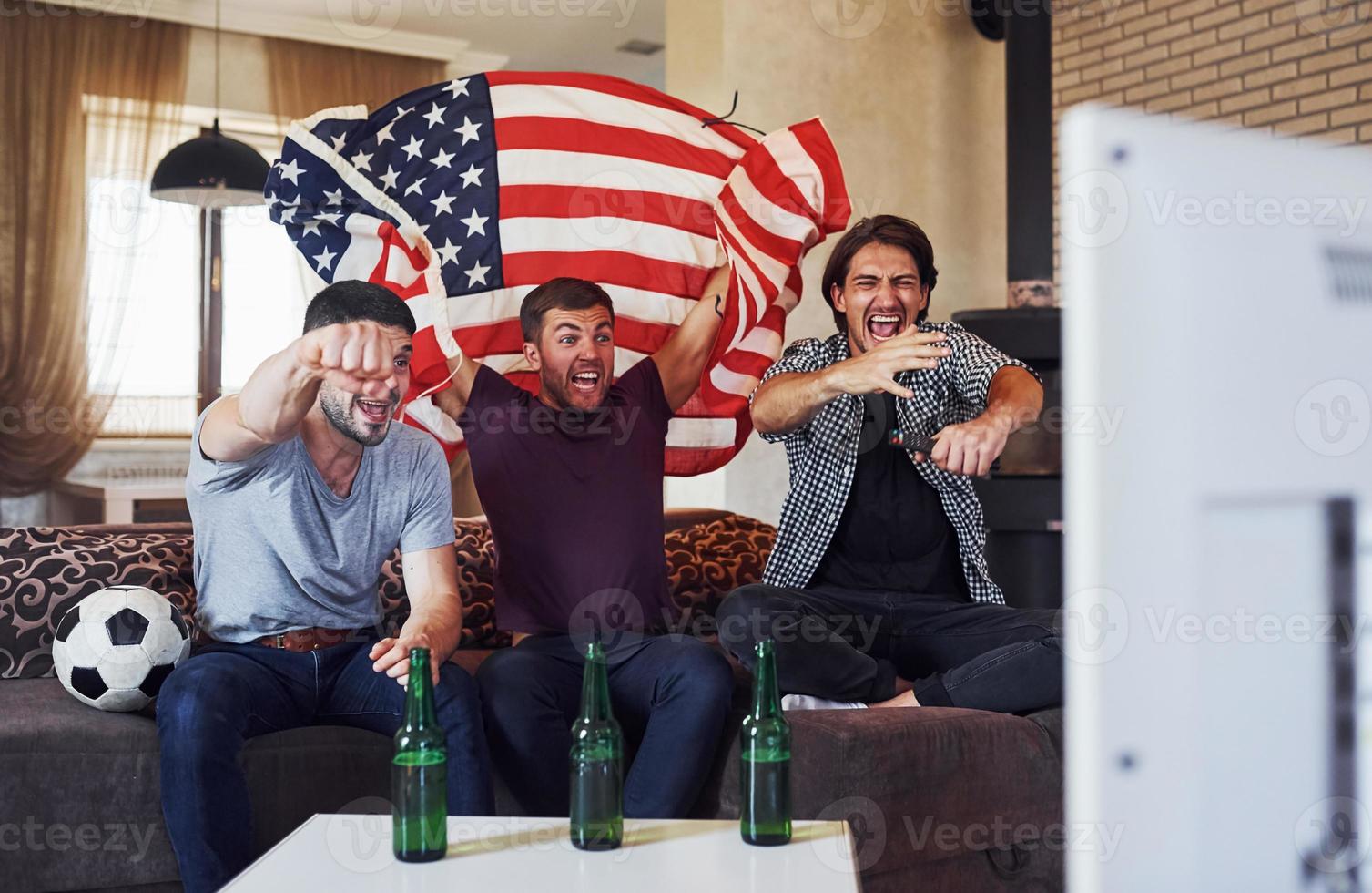 três amigos animados assistindo futebol na tv em casa juntos foto