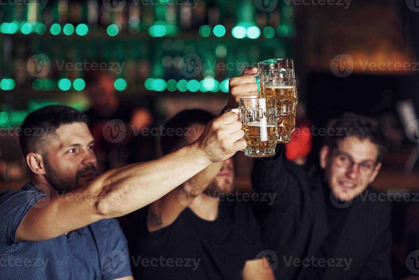 copos batendo. três fãs de esportes em um bar assistindo futebol. com cerveja nas mãos foto