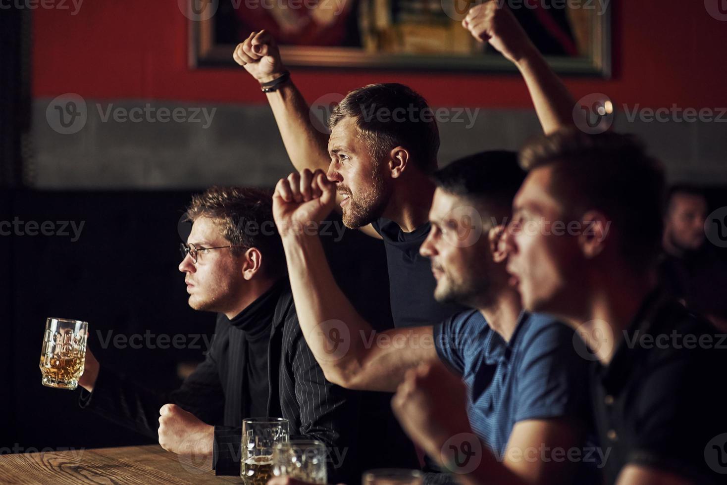 três fãs de esportes em um bar assistindo futebol. com cerveja nas mãos foto