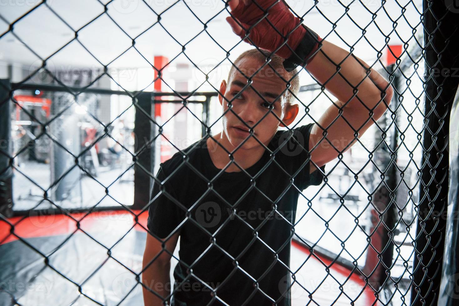 Tire uma folga. esportista no ringue de boxe tem exercício. encostado na cerca foto