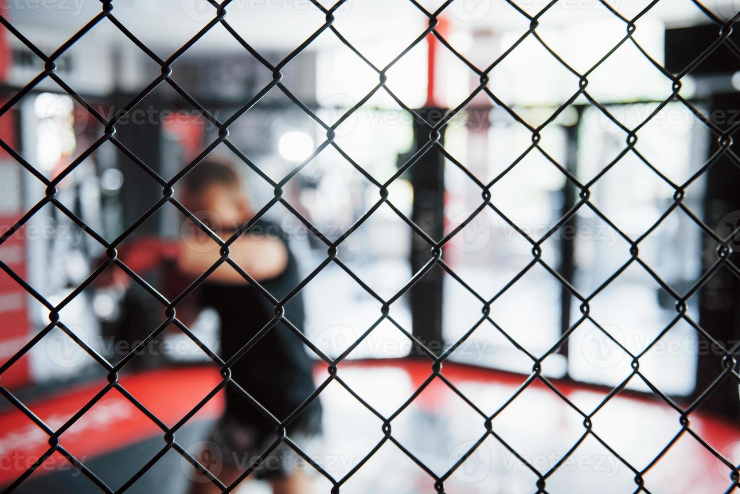 técnica de foco de imagem. jovem boxeador em bandagens vermelhas tem exercício. no ginásio na jaula foto