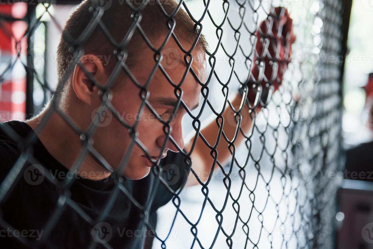 vista lateral. Tire uma folga. esportista no ringue de boxe tem exercício. encostado na cerca foto