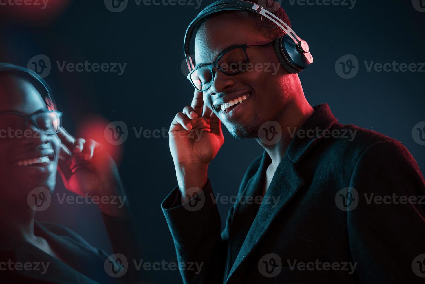 curtindo ouvir música em fones de ouvido. em copos. iluminação neon futurista. jovem afro-americano no estúdio foto