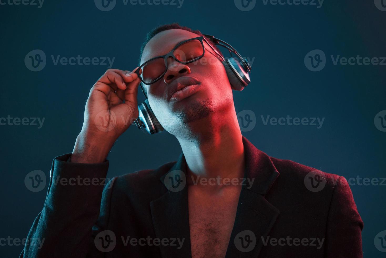 curtindo ouvir música em fones de ouvido. em copos. iluminação neon futurista. jovem afro-americano no estúdio foto