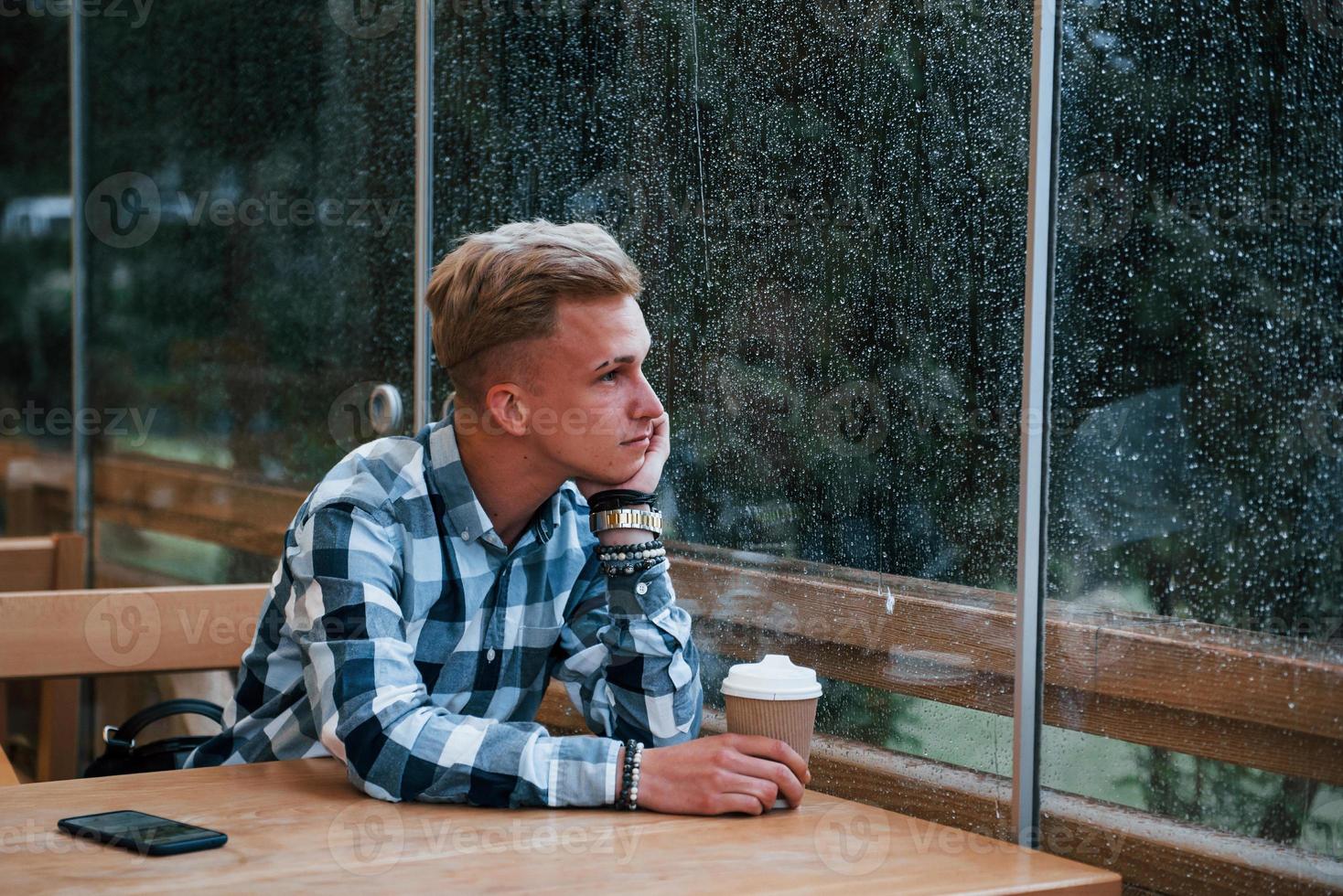 retrato do jovem estudante que se senta no café em dia chuvoso. uma pessoa foto