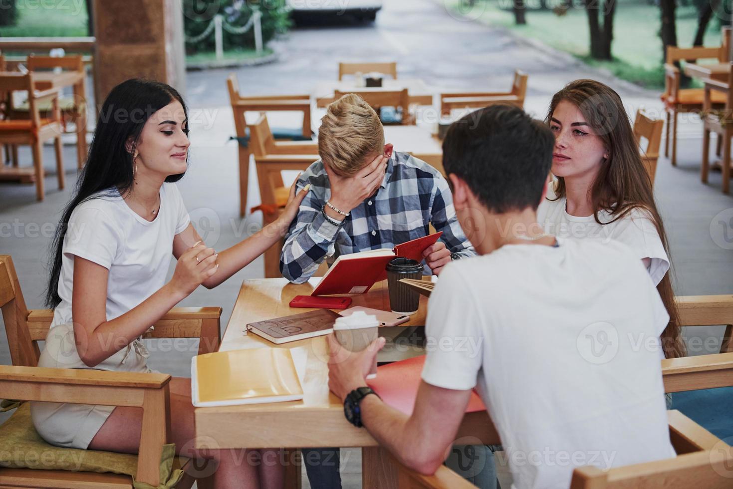 sentado no café e conversando. quatro jovens estudantes em roupas casuais se encontram em um dia chuvoso foto