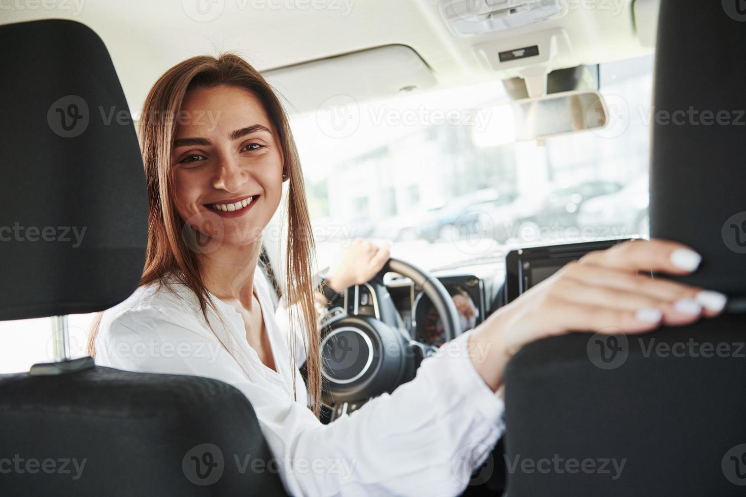 alegre motorista feminina está em seu carro novo. interior do automóvel moderno foto
