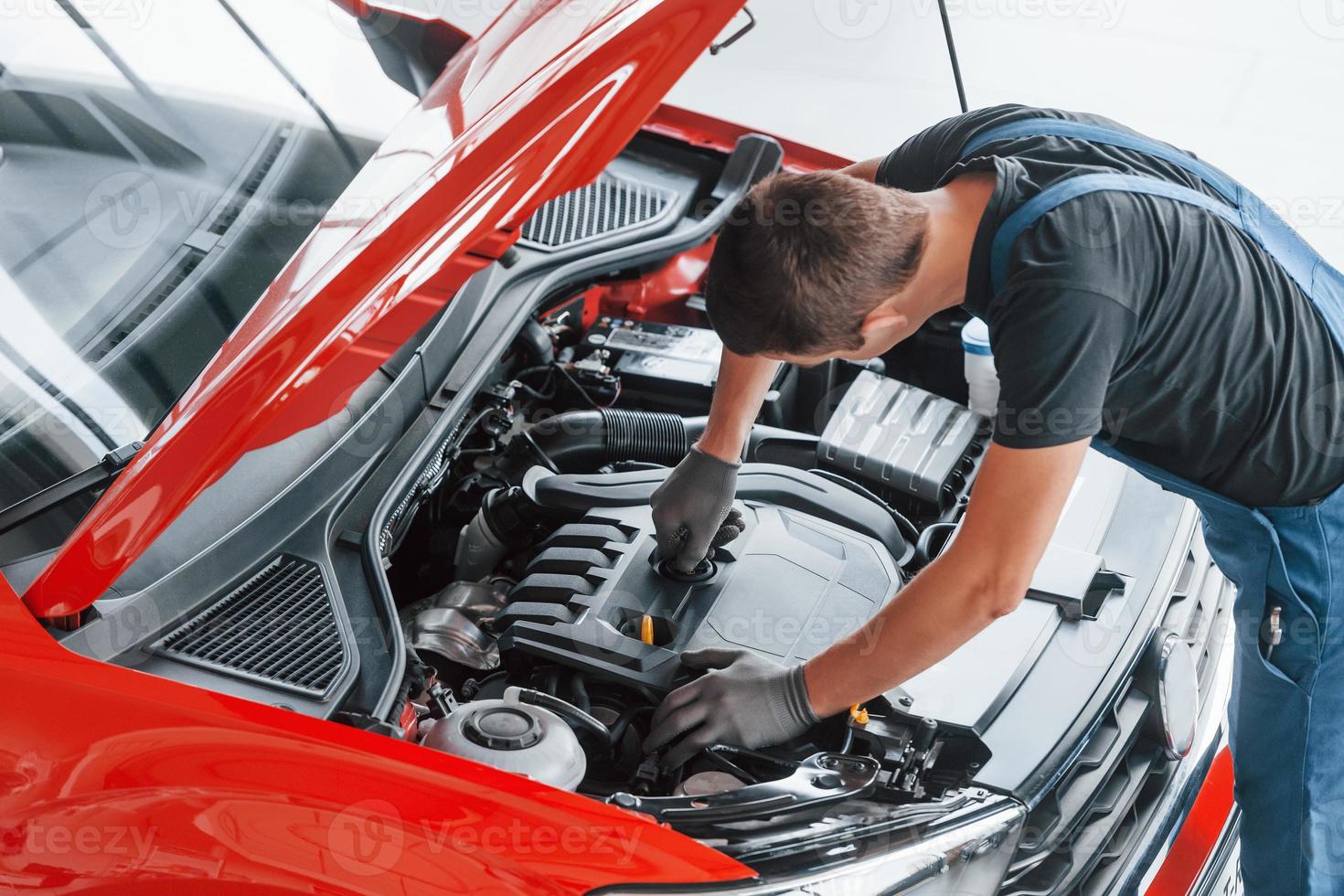 vista superior do trabalhador masculino de uniforme que conserta automóvel vermelho foto