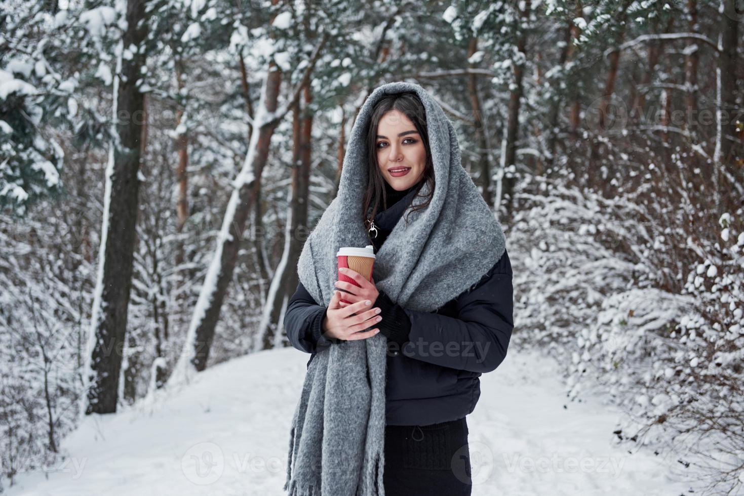 tendo bom humor. garota de roupas quentes com uma xícara de café dá um passeio na floresta de inverno foto