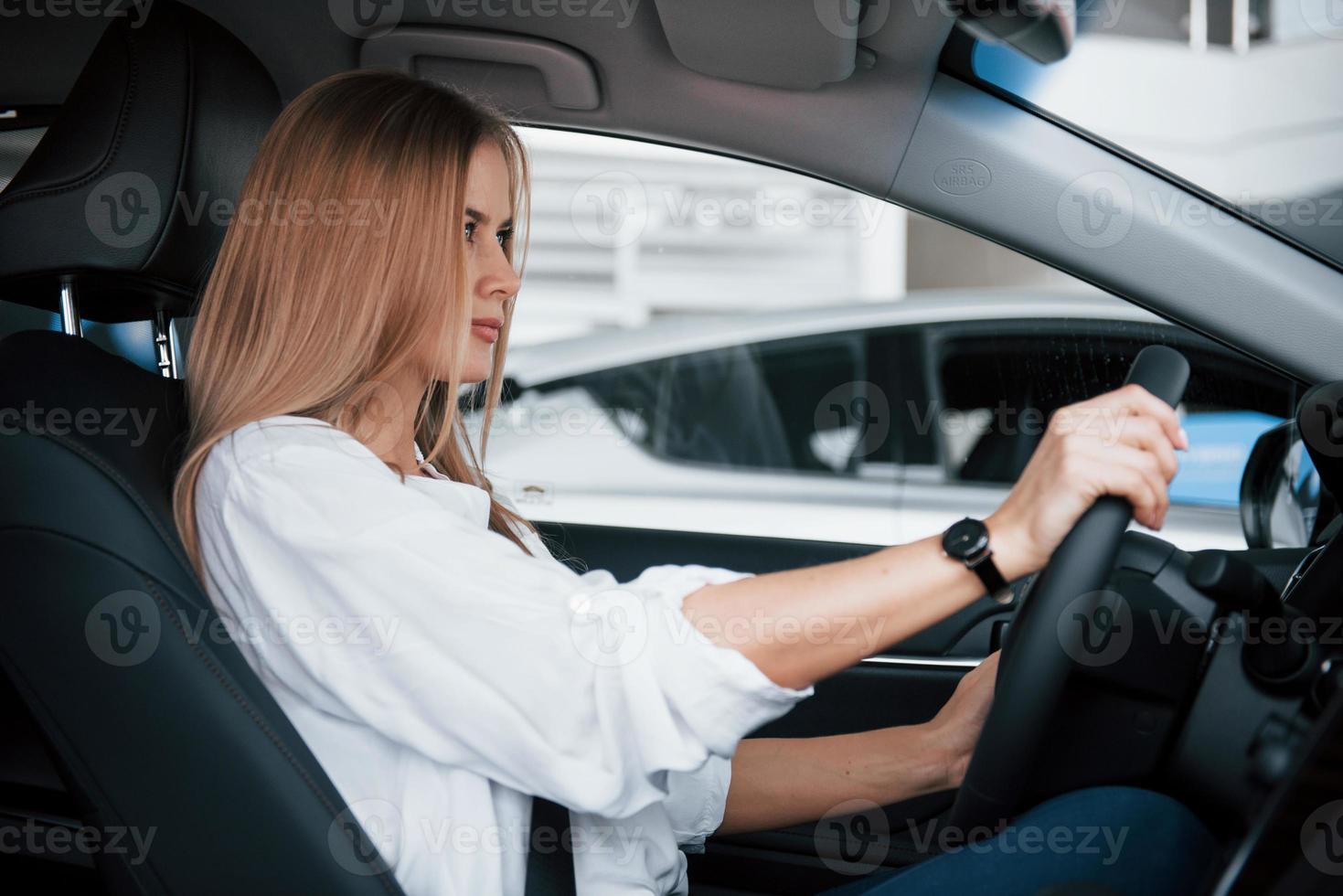 vamos dirigir. linda loira sentada no carro novo com interior preto moderno foto