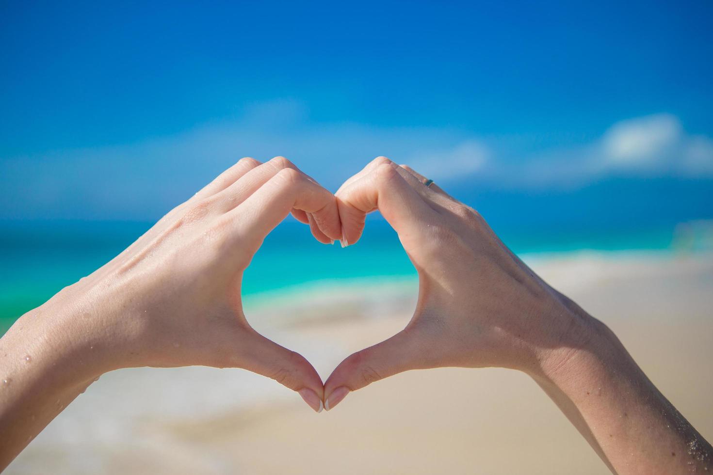 pessoa fazendo um coração com as mãos na praia foto