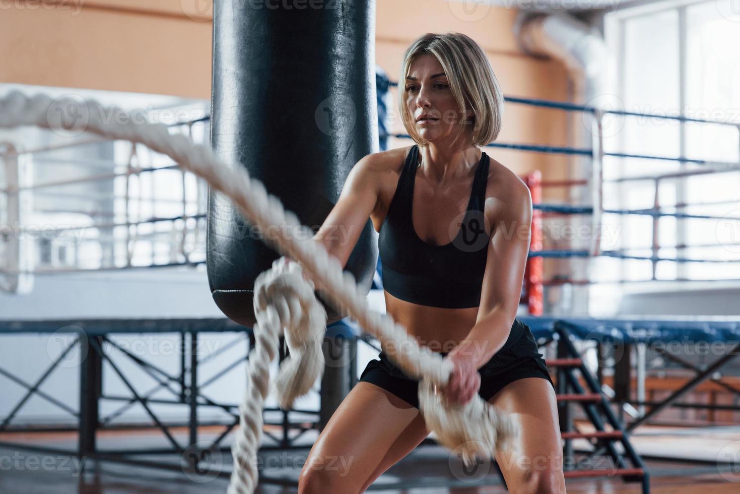 olha para a frente. mulher loira esporte tem exercício com cordas no ginásio. mulher forte foto