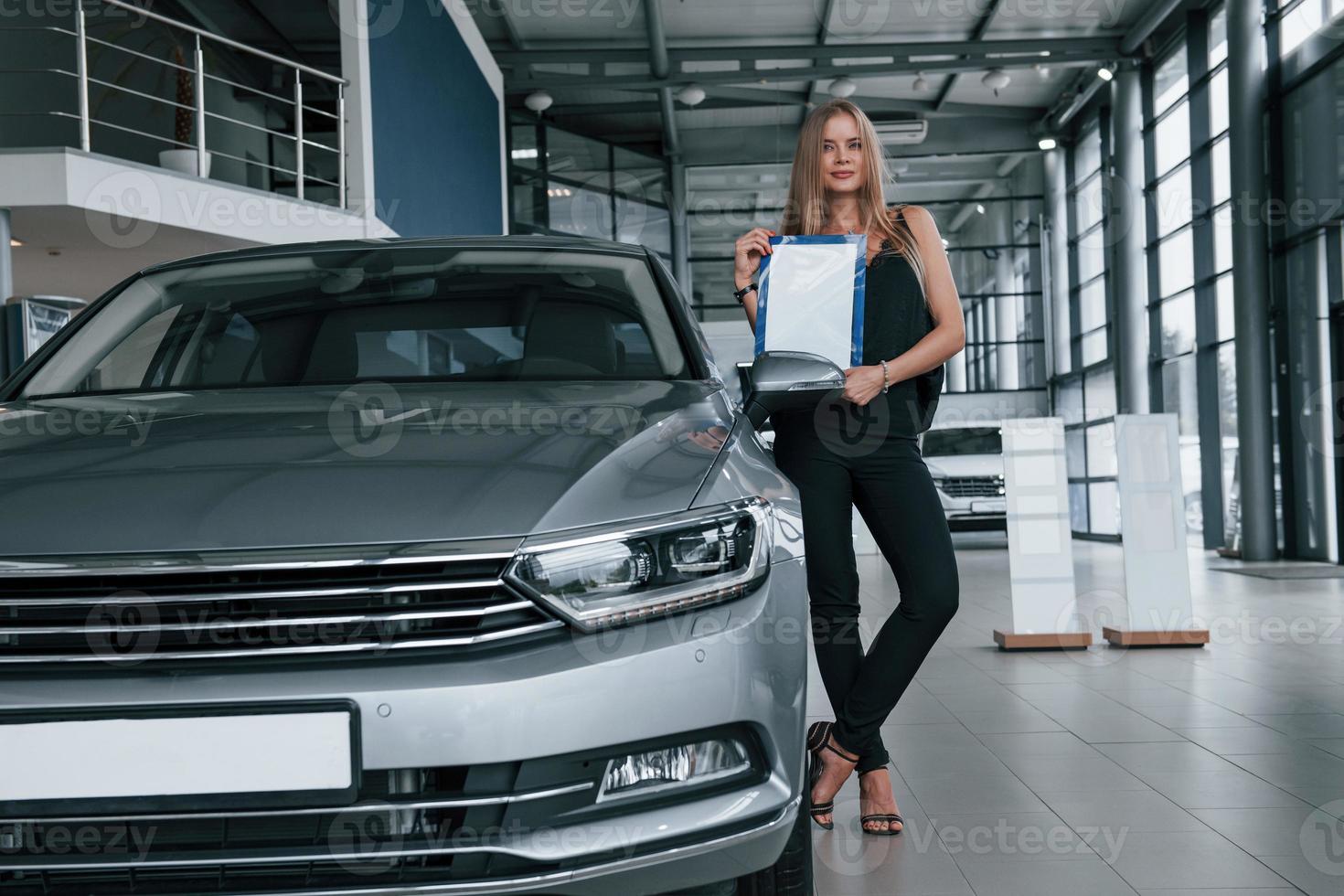 automóvel perfeitamente polido. menina e carro moderno no salão. durante o dia dentro de casa. comprando veículo novo foto