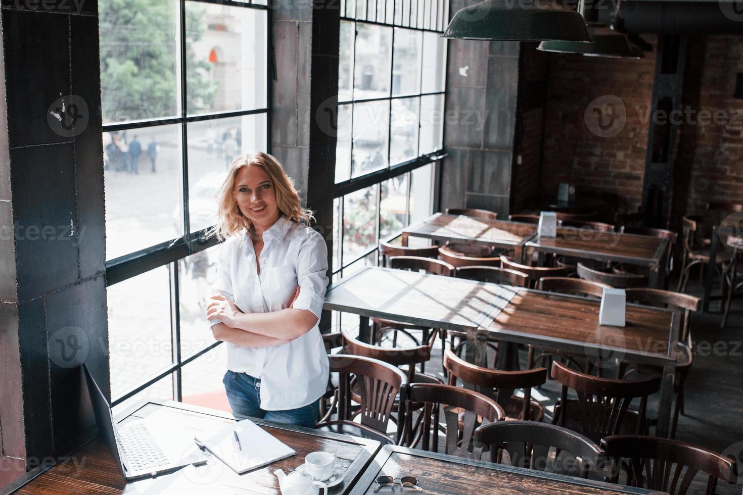 em pé com os braços cruzados. mulher de negócios com cabelo loiro encaracolado dentro de casa no café durante o dia foto