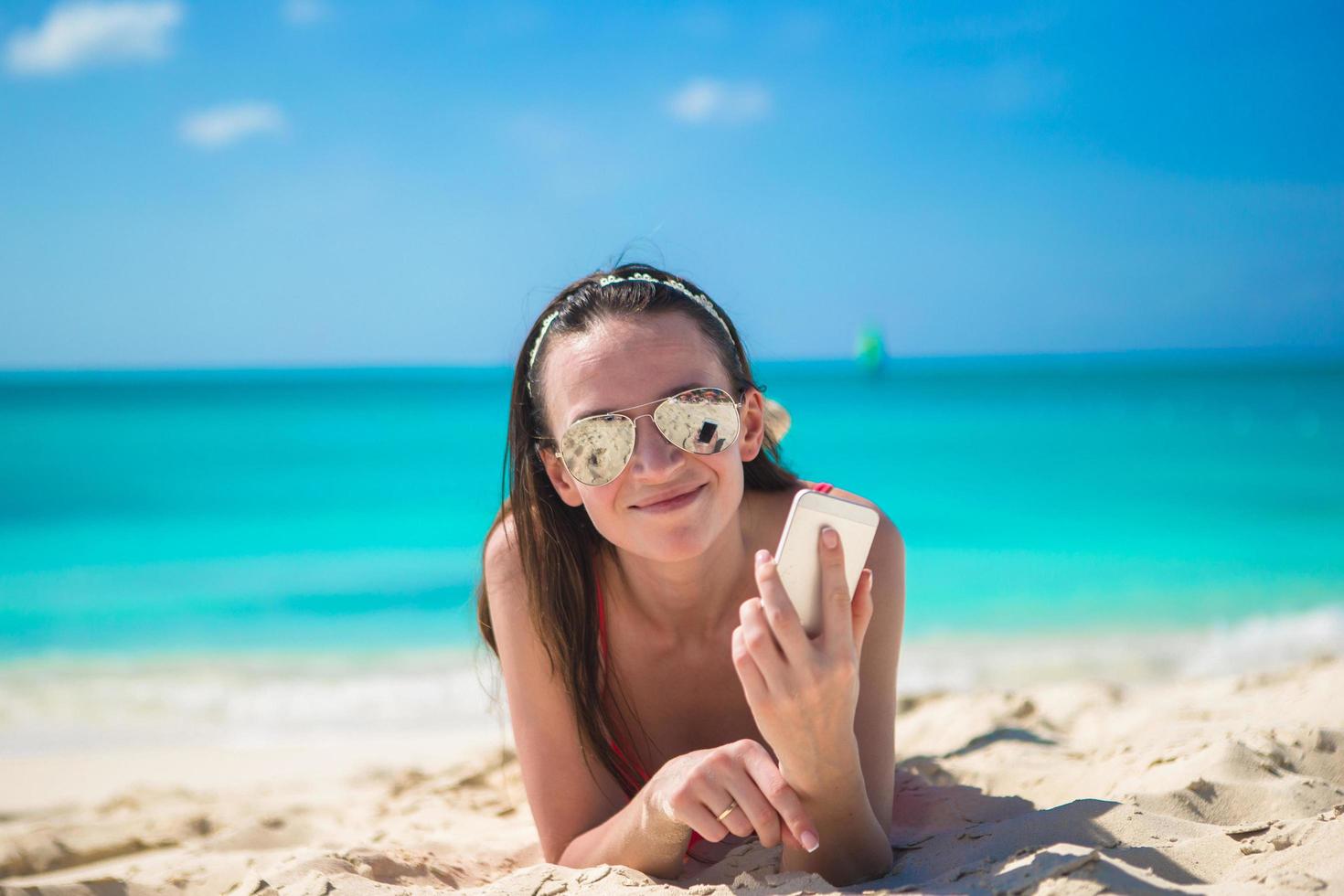 mulher deitada na praia com seu telefone foto