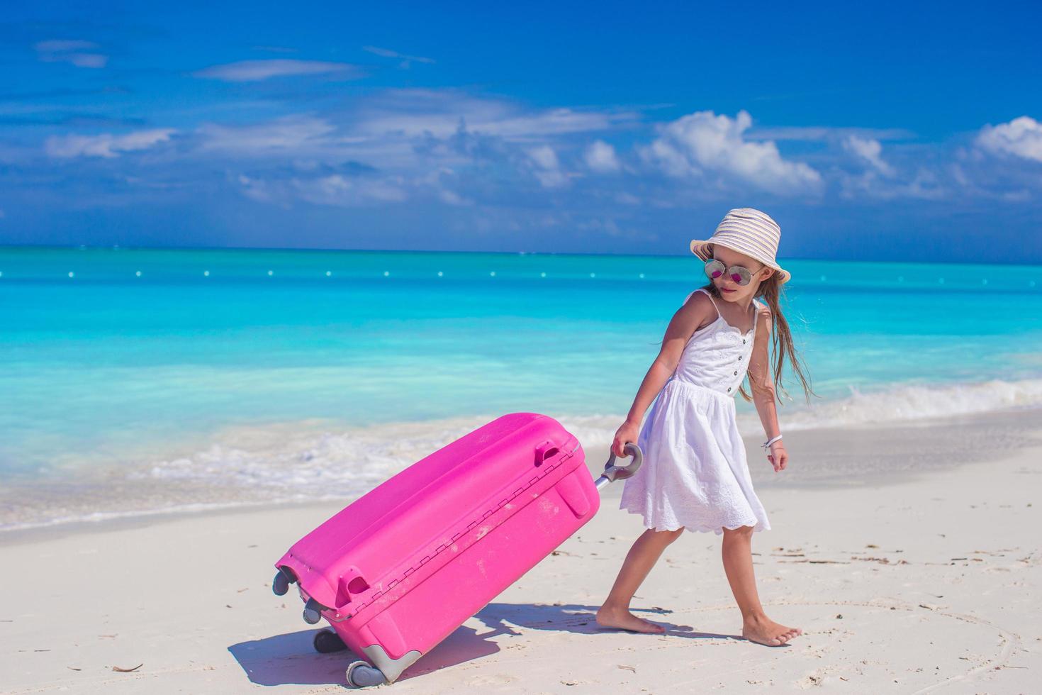 garota puxando uma mala rosa em uma praia foto