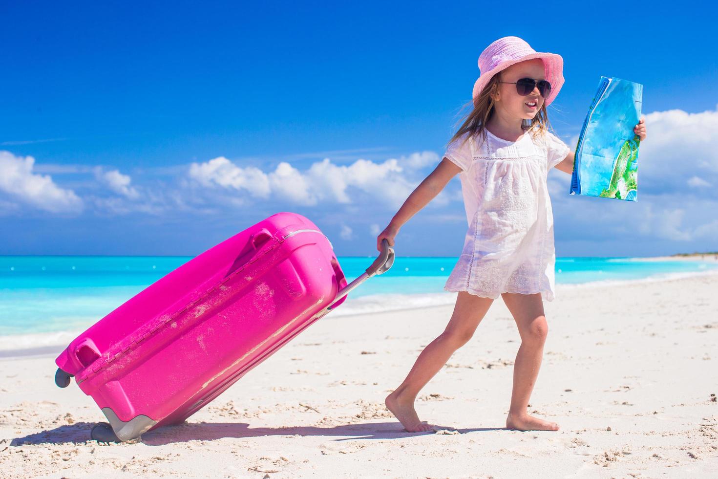 garota puxando uma mala e segurando um mapa em uma praia foto