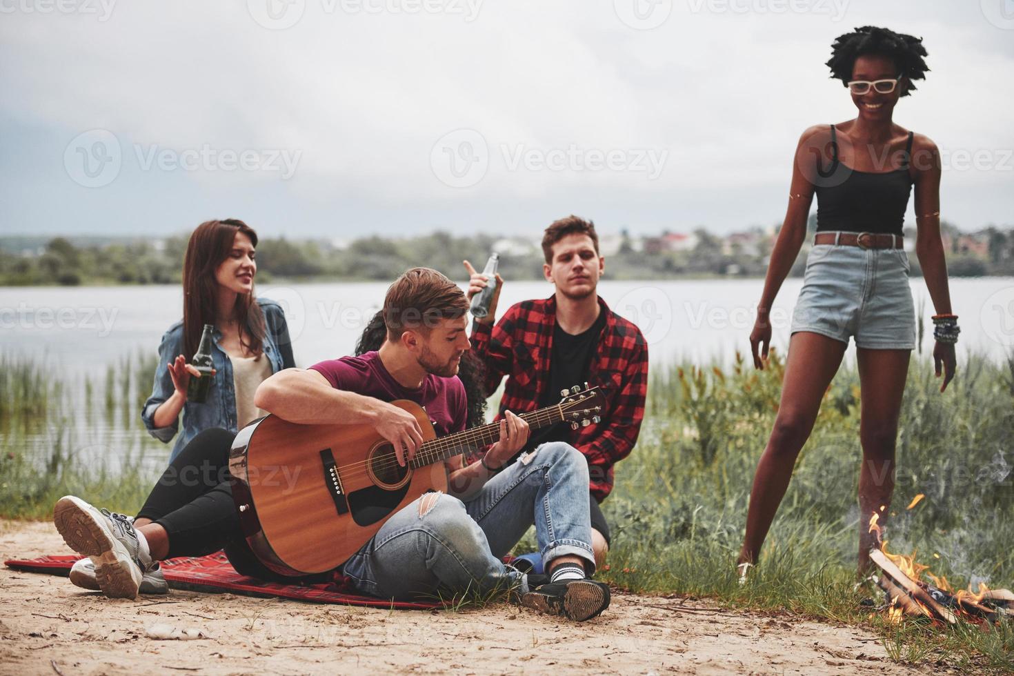 sinta a música. grupo de pessoas faz piquenique na praia. amigos se divertem no fim de semana foto