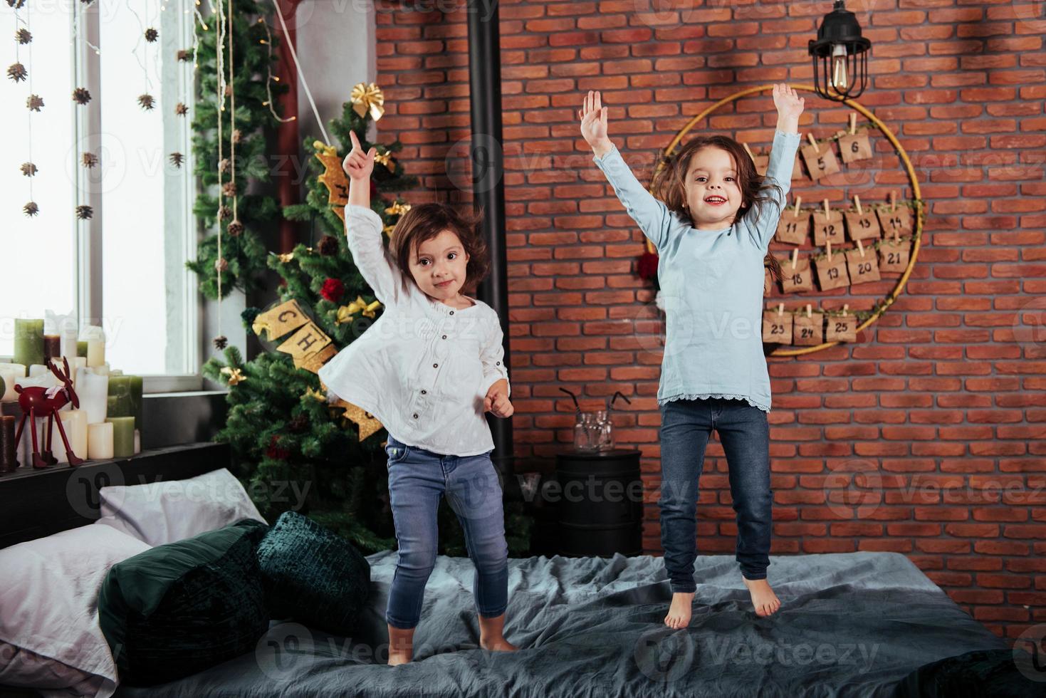 árvore de natal atrás. crianças alegres se divertindo e pulando na cama com fundo decorativo de férias foto